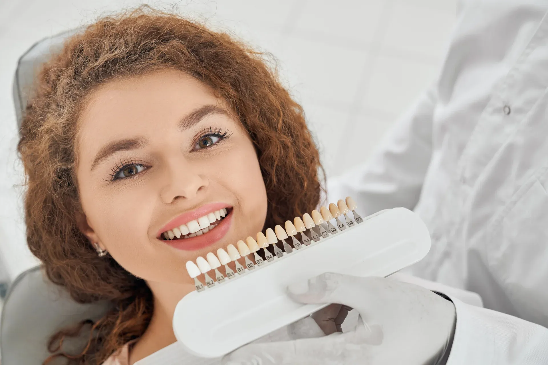 woman-smiling-while-male-dentist-keeping-teeth-color-range (1).webp